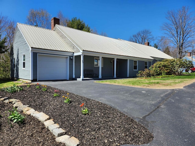 ranch-style house featuring aphalt driveway, a garage, a porch, a chimney, and metal roof