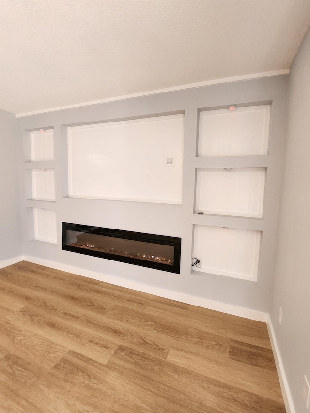 unfurnished living room with baseboards, built in features, a glass covered fireplace, and wood finished floors