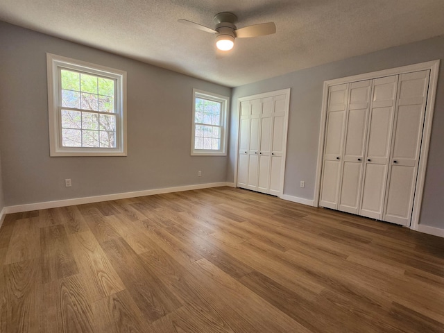 unfurnished bedroom featuring wood finished floors, two closets, baseboards, a textured ceiling, and a ceiling fan