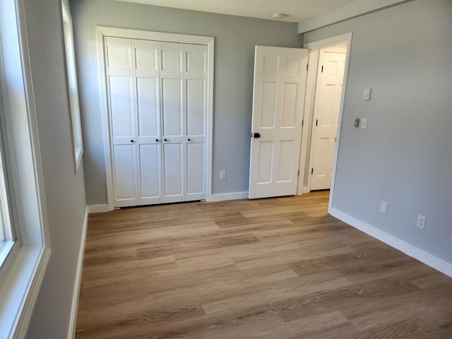 unfurnished bedroom with baseboards, light wood-style flooring, and a closet