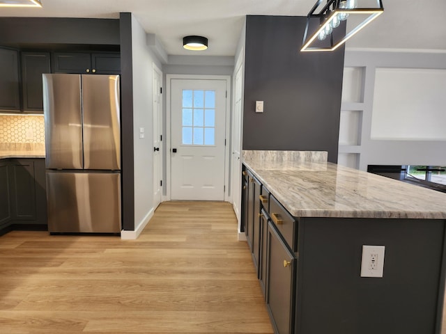 kitchen with tasteful backsplash, light wood-type flooring, light stone counters, freestanding refrigerator, and a peninsula