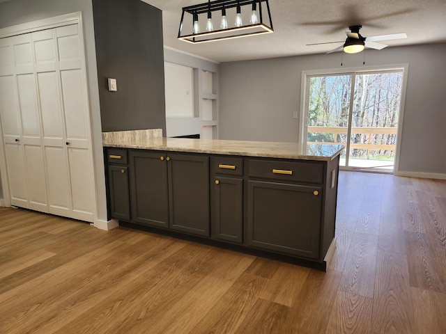 kitchen featuring a peninsula, light stone countertops, gray cabinets, a ceiling fan, and light wood finished floors