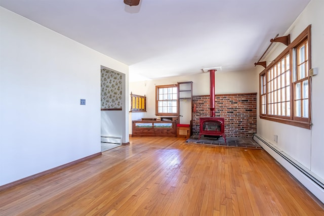 unfurnished living room with hardwood / wood-style flooring, a baseboard heating unit, baseboard heating, and a wood stove