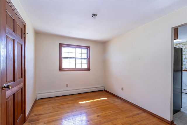 unfurnished bedroom with baseboards, a baseboard heating unit, and light wood-style flooring