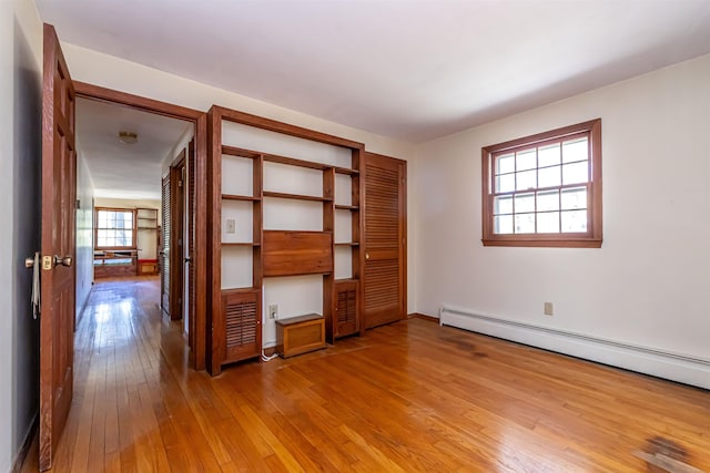 unfurnished bedroom with wood-type flooring, a baseboard radiator, baseboards, and a closet
