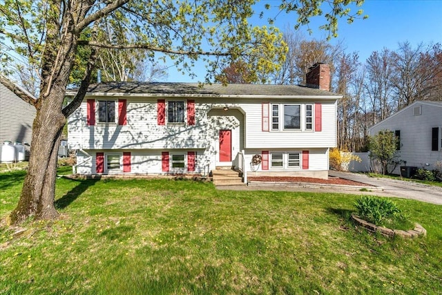 raised ranch with a front lawn, a chimney, and entry steps