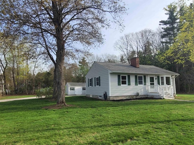 view of front facade featuring a chimney, a shingled roof, a front yard, and a shed