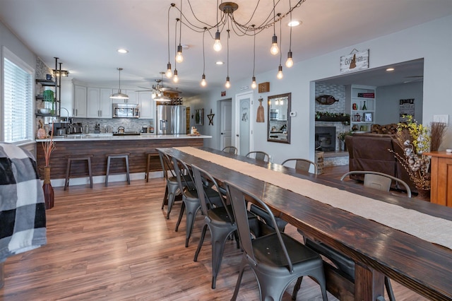 dining area with a fireplace, ceiling fan with notable chandelier, recessed lighting, and wood finished floors