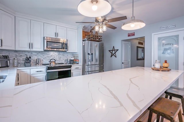 kitchen featuring ceiling fan, appliances with stainless steel finishes, tasteful backsplash, white cabinets, and a breakfast bar