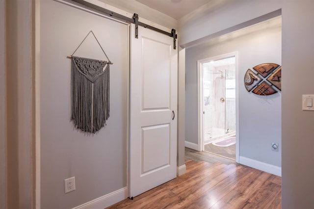 hall with baseboards, a barn door, and light wood-style flooring