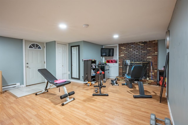 exercise area with baseboards, baseboard heating, a brick fireplace, and light wood-type flooring