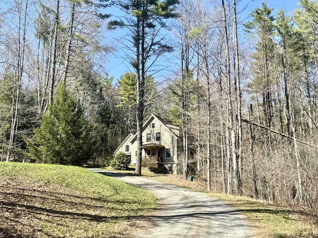 rustic home featuring stucco siding, a forest view, and aphalt driveway