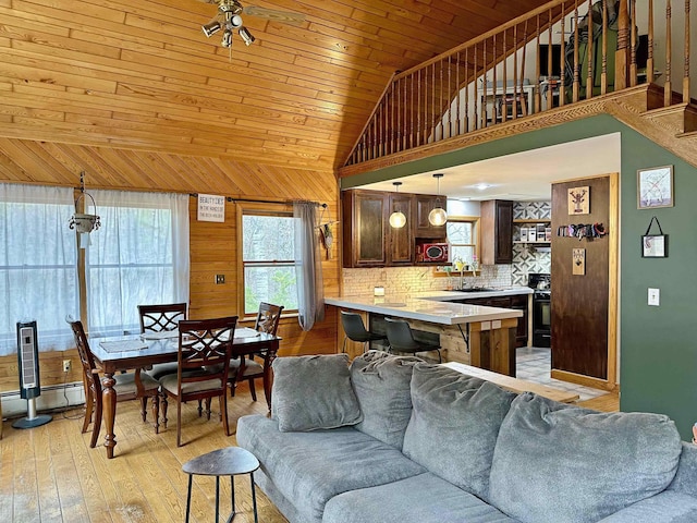 living room with wooden walls, baseboard heating, light wood finished floors, high vaulted ceiling, and wooden ceiling