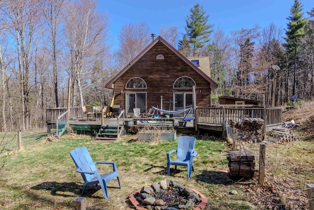 rear view of property with a lawn, a wooden deck, and a fire pit