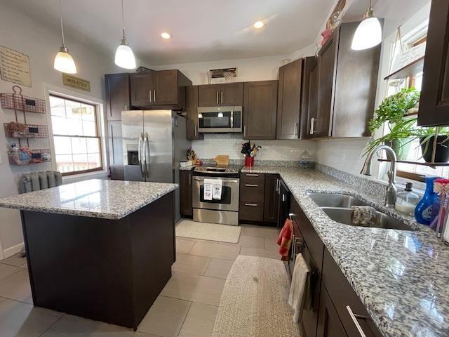kitchen featuring light stone countertops, dark brown cabinets, tasteful backsplash, a sink, and stainless steel appliances