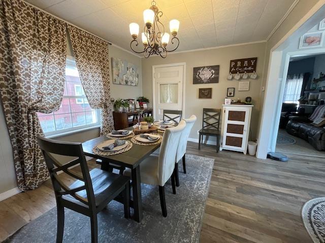 dining space with baseboards, an inviting chandelier, ornamental molding, and wood finished floors