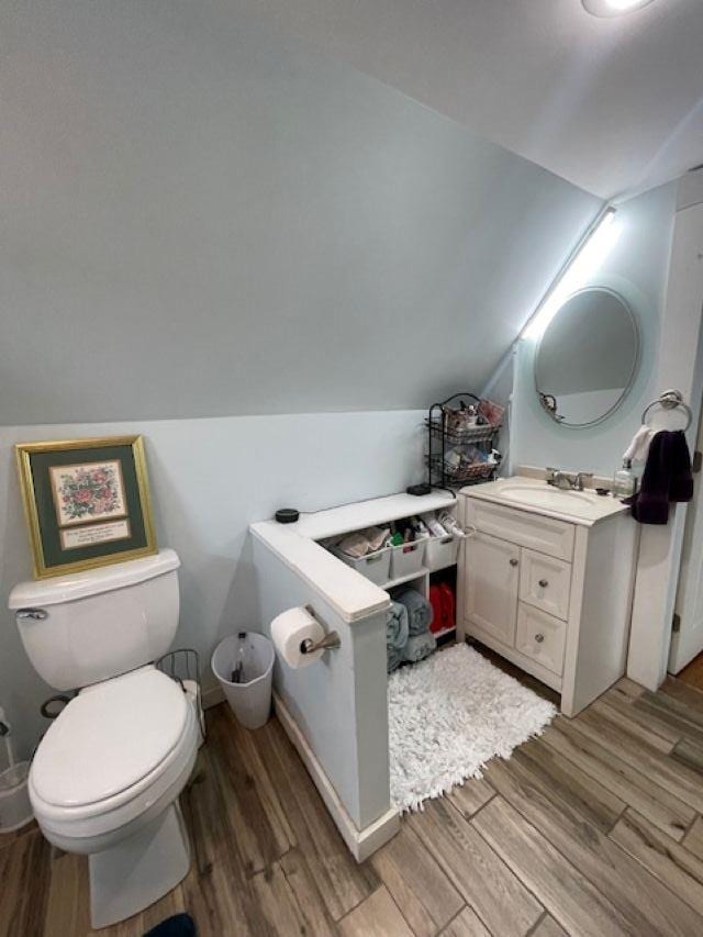 bathroom featuring vanity, toilet, wood finished floors, and lofted ceiling