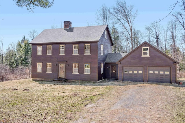 colonial house with a garage, roof with shingles, a chimney, entry steps, and driveway