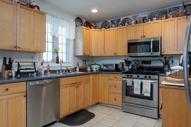 kitchen featuring light brown cabinets, dark countertops, a sink, light tile patterned floors, and stainless steel appliances