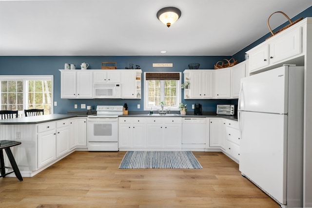 kitchen featuring white appliances, a peninsula, dark countertops, and white cabinets