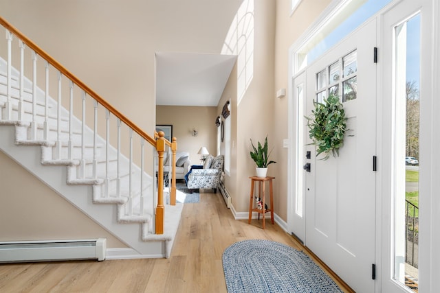 foyer featuring a high ceiling, a baseboard radiator, stairs, and wood finished floors