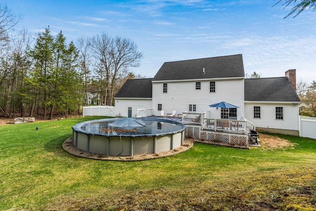 back of property featuring a shingled roof, a covered pool, a wooden deck, a chimney, and a yard