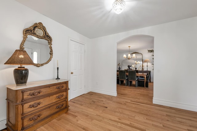 interior space with baseboards, arched walkways, light wood finished floors, and a chandelier