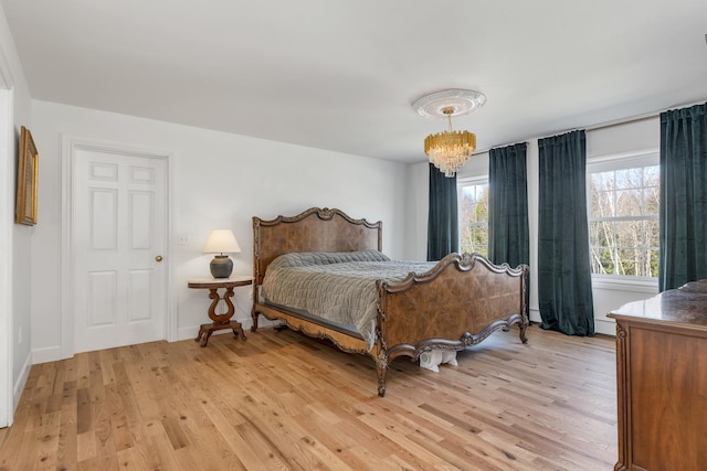 bedroom with light wood-style floors, baseboards, a baseboard heating unit, and an inviting chandelier