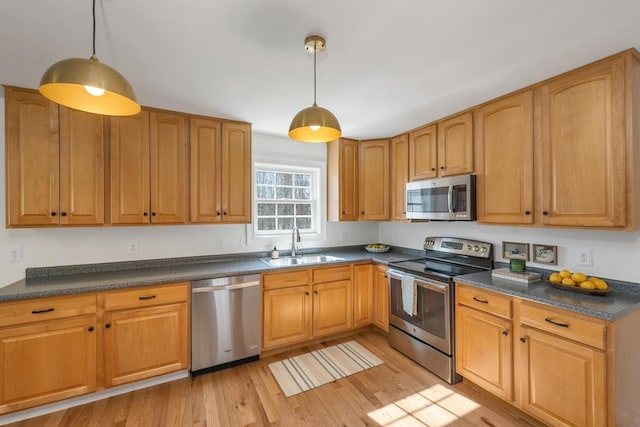 kitchen featuring dark countertops, light wood-style floors, a sink, appliances with stainless steel finishes, and hanging light fixtures