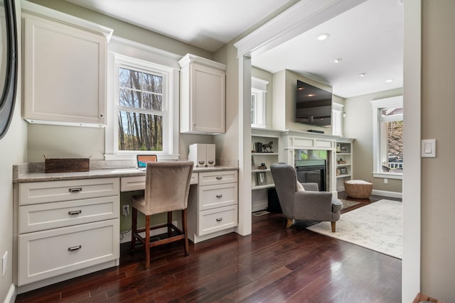 office space with a premium fireplace, dark wood-style floors, built in desk, and a wealth of natural light