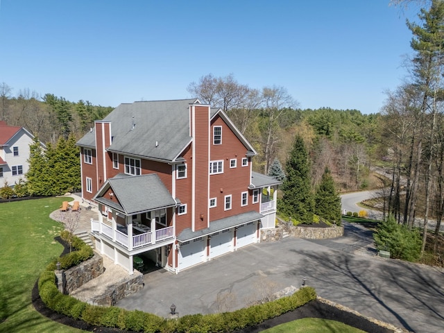 back of house with a garage, aphalt driveway, a chimney, and a forest view