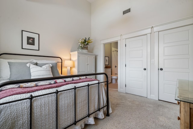 bedroom with light colored carpet, ensuite bath, a high ceiling, and visible vents