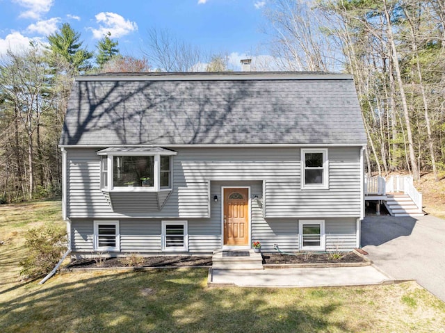 raised ranch with a shingled roof, a front yard, and a gambrel roof