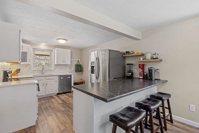 kitchen featuring a peninsula, a textured ceiling, appliances with stainless steel finishes, and a kitchen bar