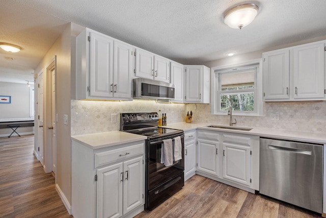 kitchen with appliances with stainless steel finishes, wood finished floors, a sink, light countertops, and white cabinetry