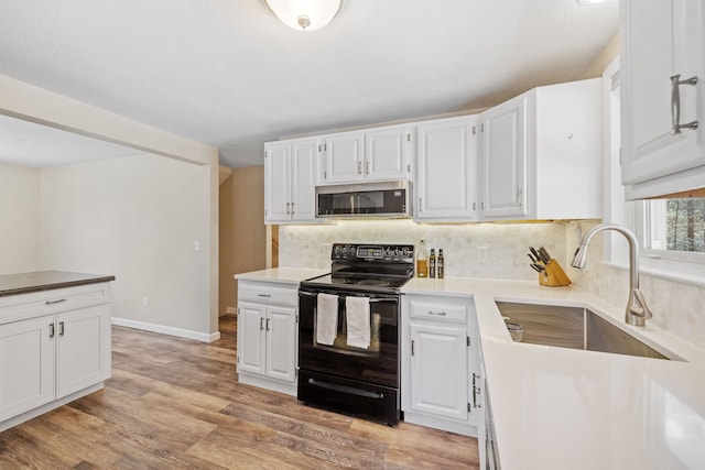 kitchen with decorative backsplash, black range with electric stovetop, a sink, stainless steel microwave, and white cabinetry