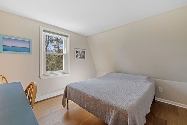 bedroom with baseboards, a baseboard heating unit, and wood finished floors