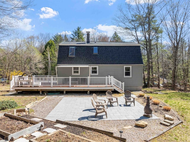 rear view of house with roof with shingles, a patio, a chimney, and a deck