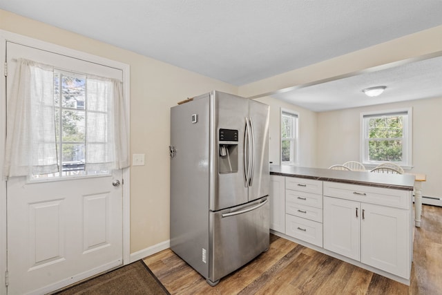 kitchen with dark countertops, stainless steel fridge with ice dispenser, white cabinets, and light wood-style flooring