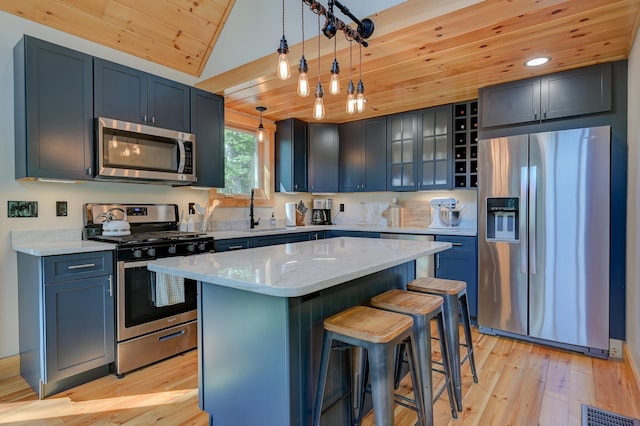 kitchen featuring appliances with stainless steel finishes, a sink, a breakfast bar area, light wood-type flooring, and wood ceiling