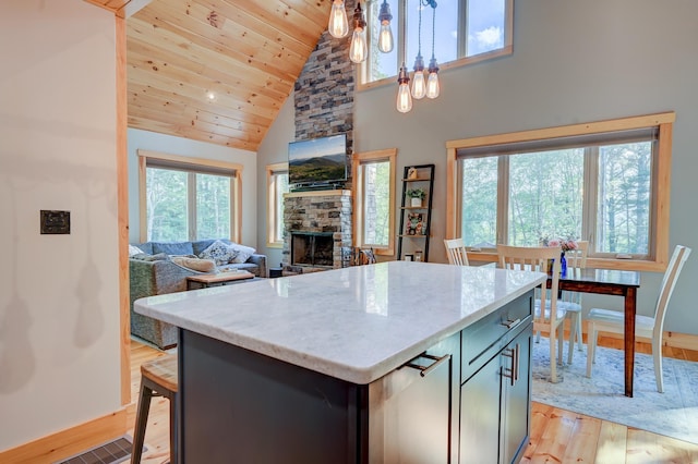 kitchen featuring light wood finished floors, high vaulted ceiling, a stone fireplace, a center island, and baseboards