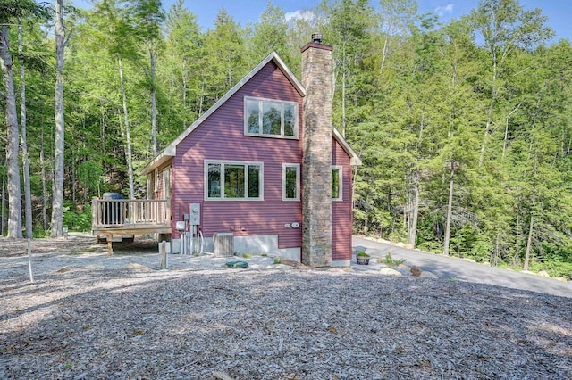 exterior space with a wooden deck, a chimney, cooling unit, and a forest view