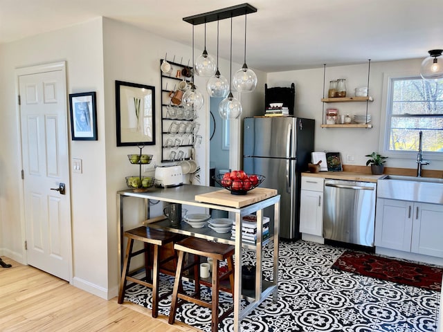 kitchen featuring a sink, baseboards, stainless steel appliances, and light wood-style flooring