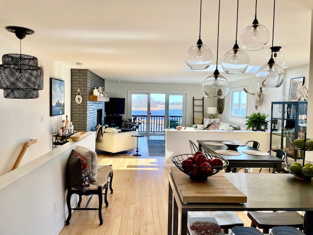 dining area with light wood-style floors, a brick fireplace, and a healthy amount of sunlight