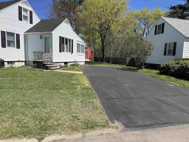 view of side of property with roof with shingles, fence, a yard, and aphalt driveway