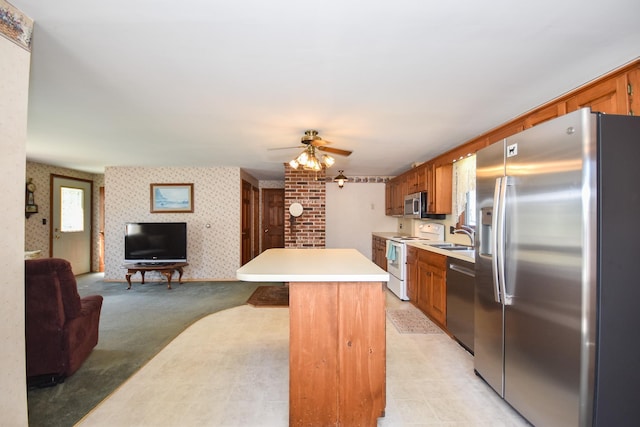 kitchen featuring open floor plan, wallpapered walls, light countertops, a sink, and appliances with stainless steel finishes