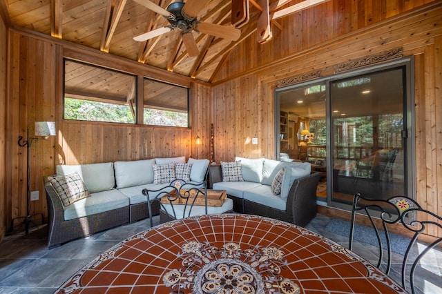 living area with ceiling fan, lofted ceiling with beams, wood walls, stone finish flooring, and wooden ceiling
