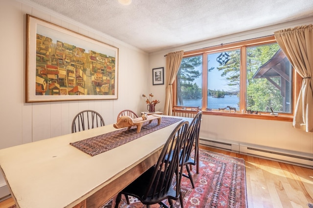 dining space featuring wood-type flooring, a textured ceiling, crown molding, and a baseboard radiator