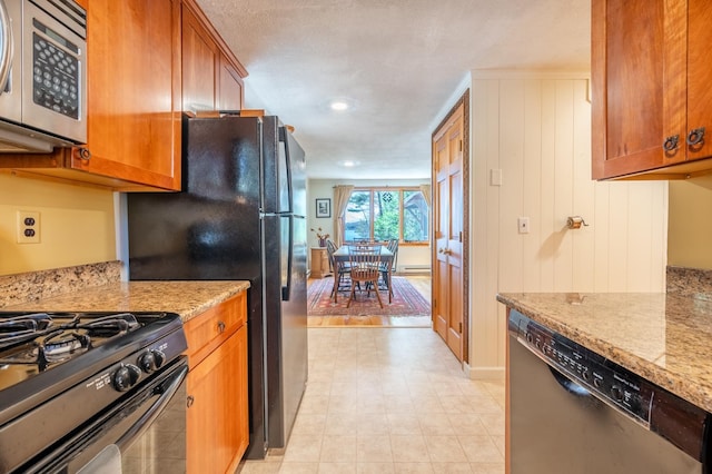 kitchen with brown cabinetry, light floors, light stone counters, and black appliances