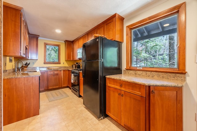 kitchen featuring brown cabinetry, a sink, light stone counters, black appliances, and ornamental molding